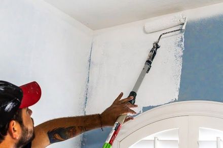 Person painting a white wall above a doorway with a roller in a blue room
