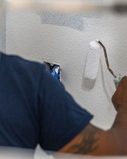 Person painting a white wall with a small roller brush