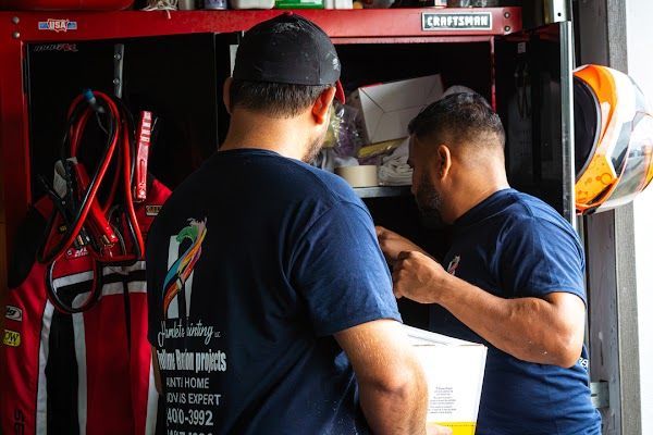Two firefighters in navy shirts stand inside a red fire truck, checking equipment in a station bay.