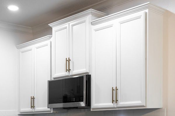 White kitchen cabinets above a black microwave with gold handles and bright ceiling lights