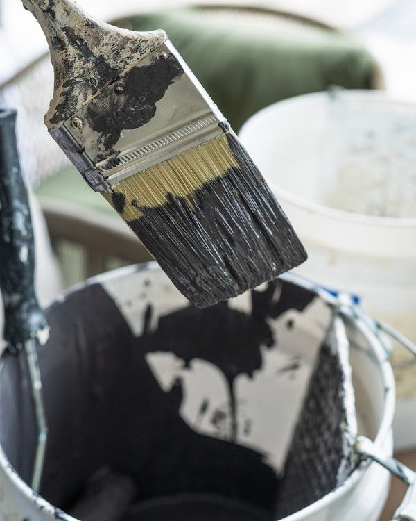 Paintbrush dripping black paint over a paint bucket