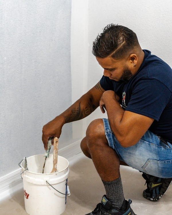 Man painting a wall corner while kneeling beside a white paint bucket
