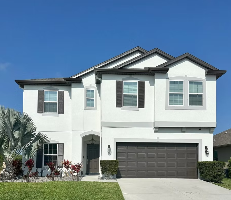 Two-story white suburban house with gray garage door and green lawn under blue sky