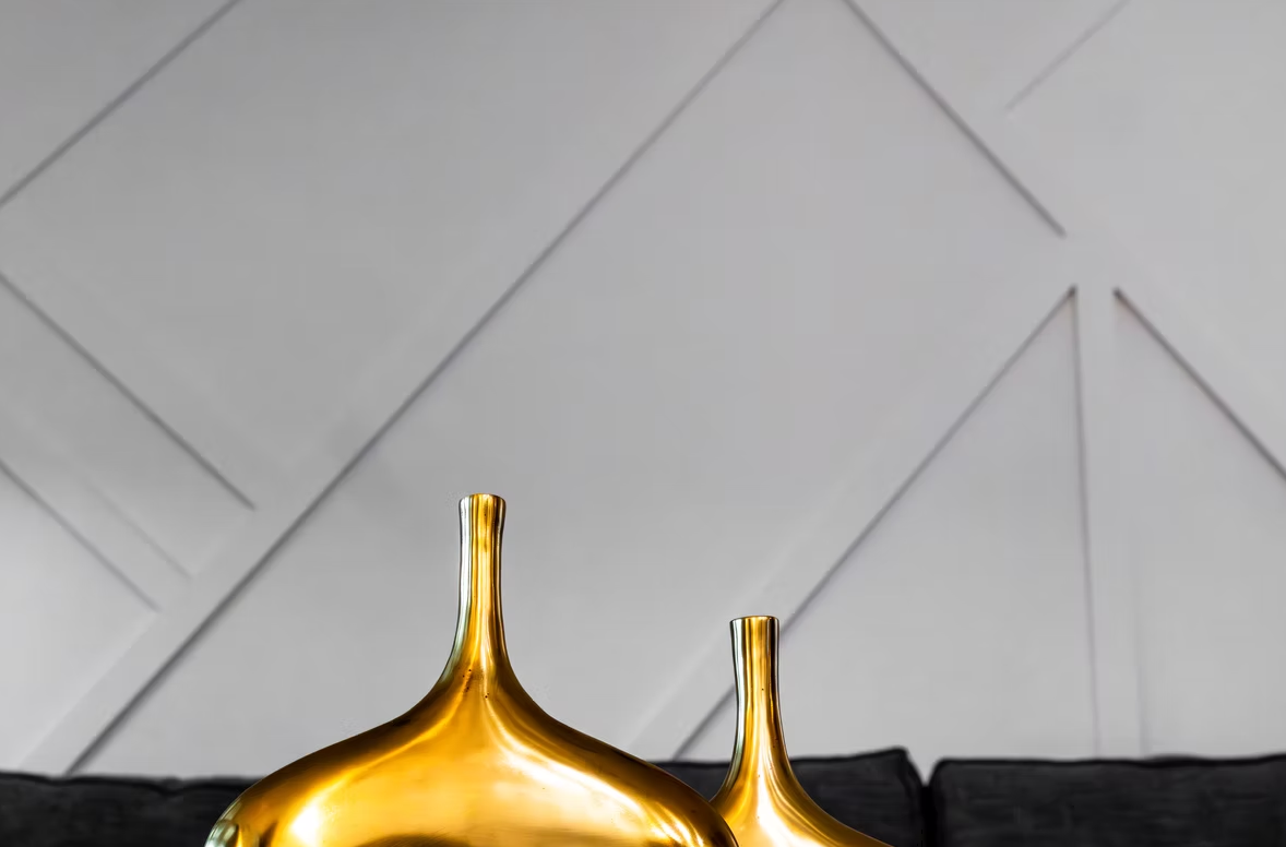 Two gold decorative vases on a black surface against a gray geometric wall
