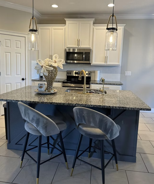 Modern kitchen with granite island, two gray stools, white cabinets, and pendant lights