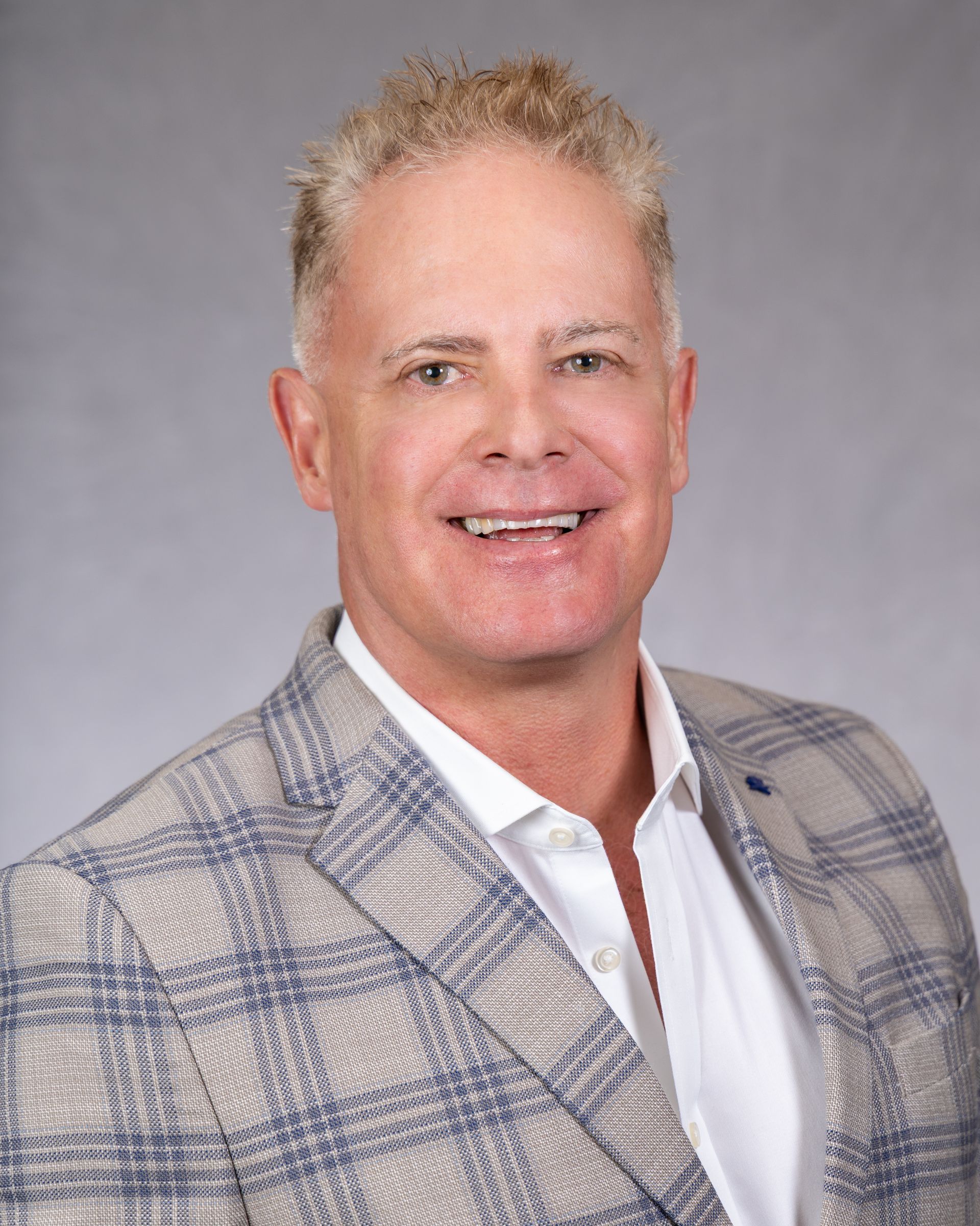 Smiling man in a white shirt and plaid blazer against a gray backdrop