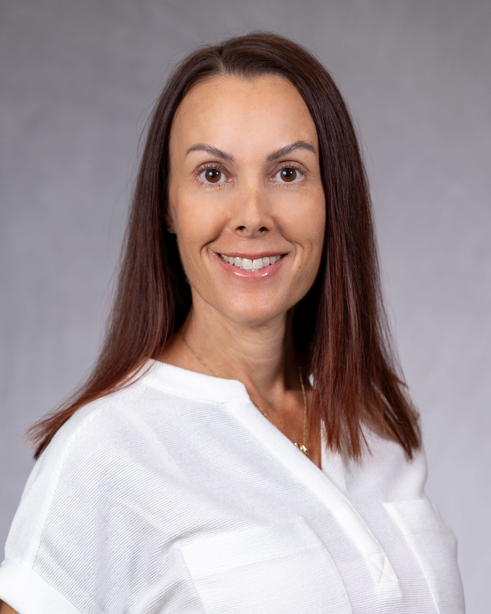 Portrait of a smiling person with long brown hair wearing a white top against a gray background