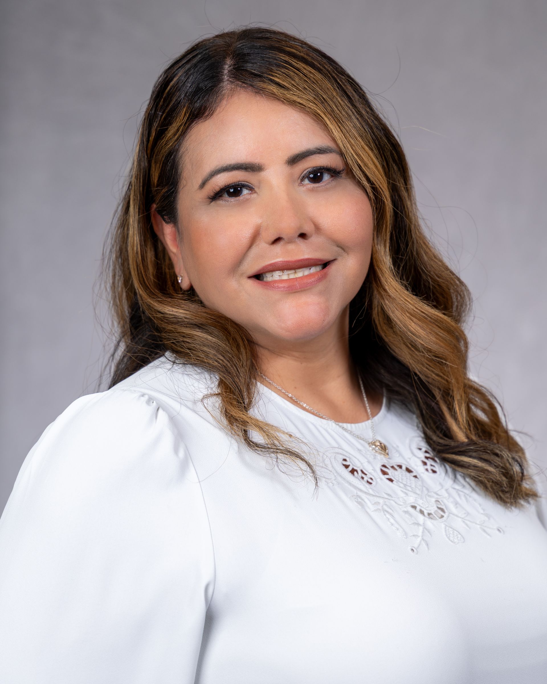 Studio portrait of a smiling woman in a white blouse against a gray background