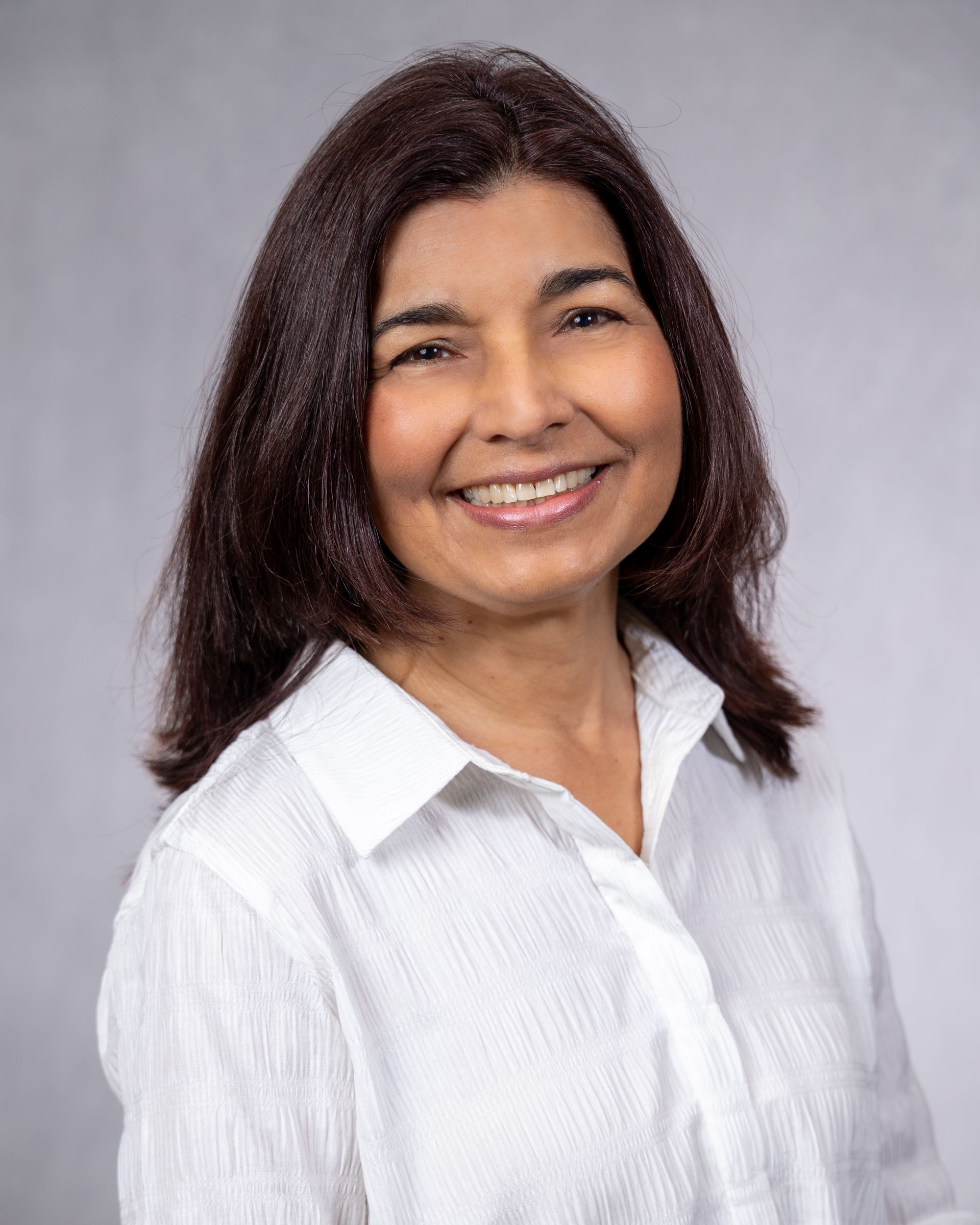 Smiling woman in a white blouse against a gray studio backdrop