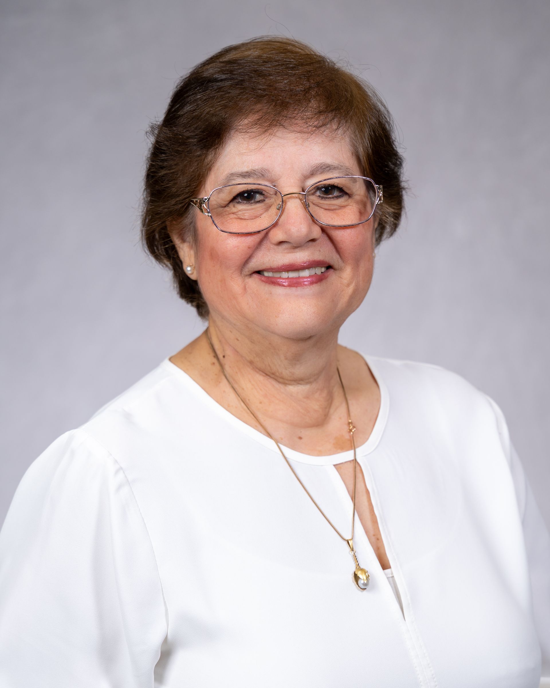 Smiling woman in glasses wearing a white blouse against a gray studio background