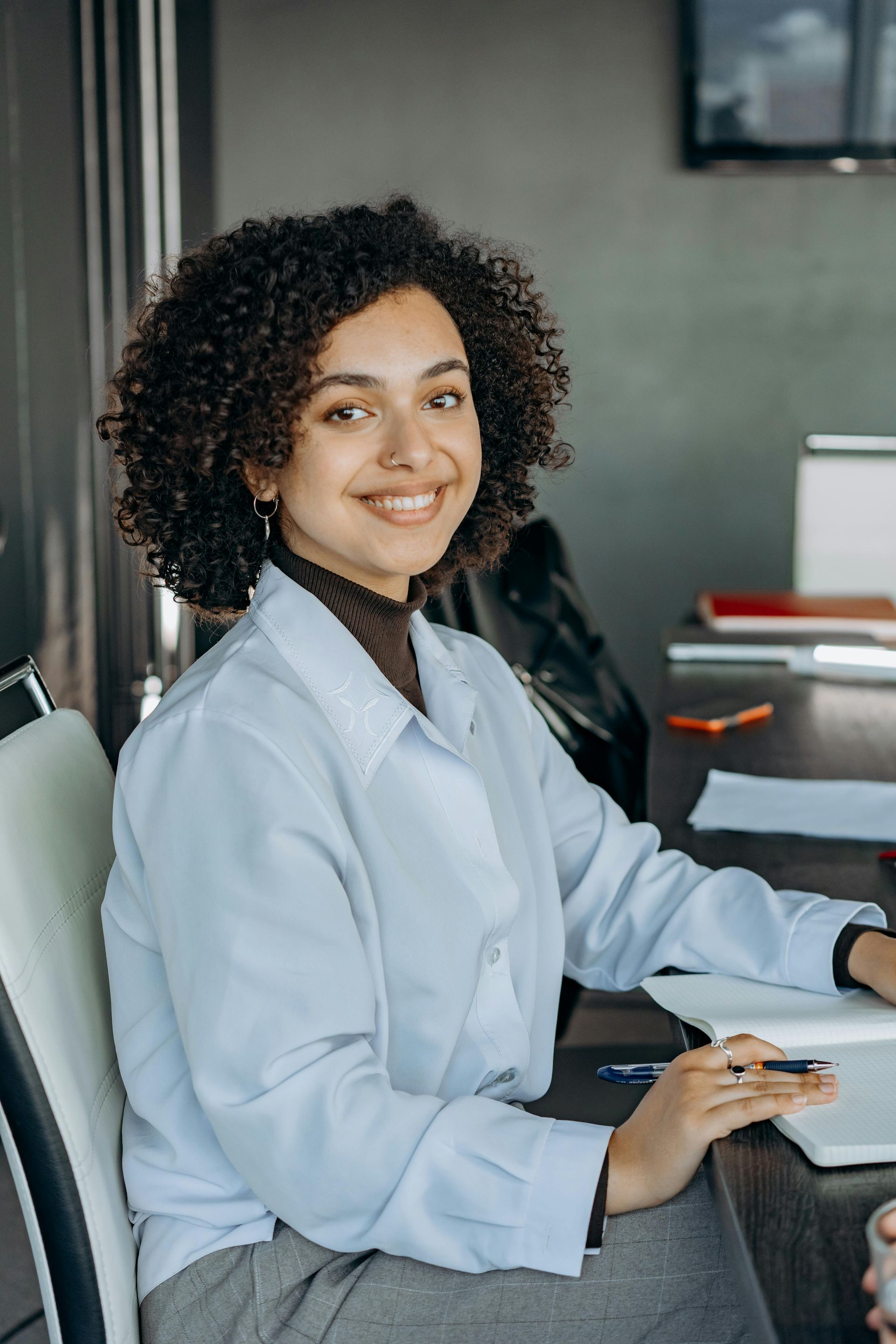 Smiling person in a light blue shirt seated at a desk in an office, typing on a keyboard.