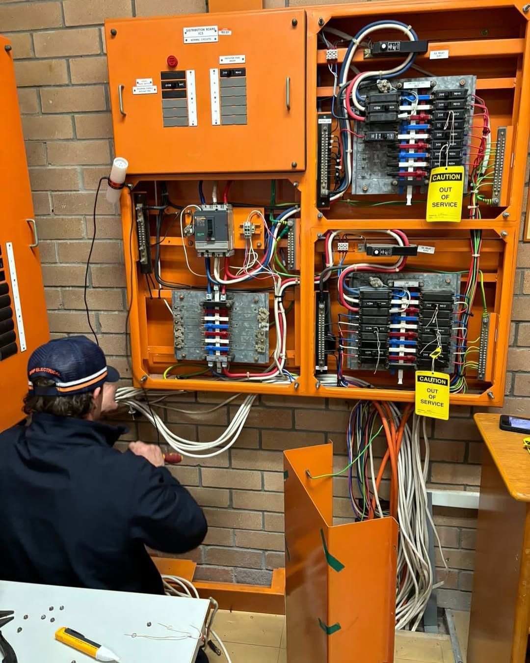 An Electrician Works on An Open Orange Electrical Panel — DMP Electrical Contractors In Mandalong, NSW