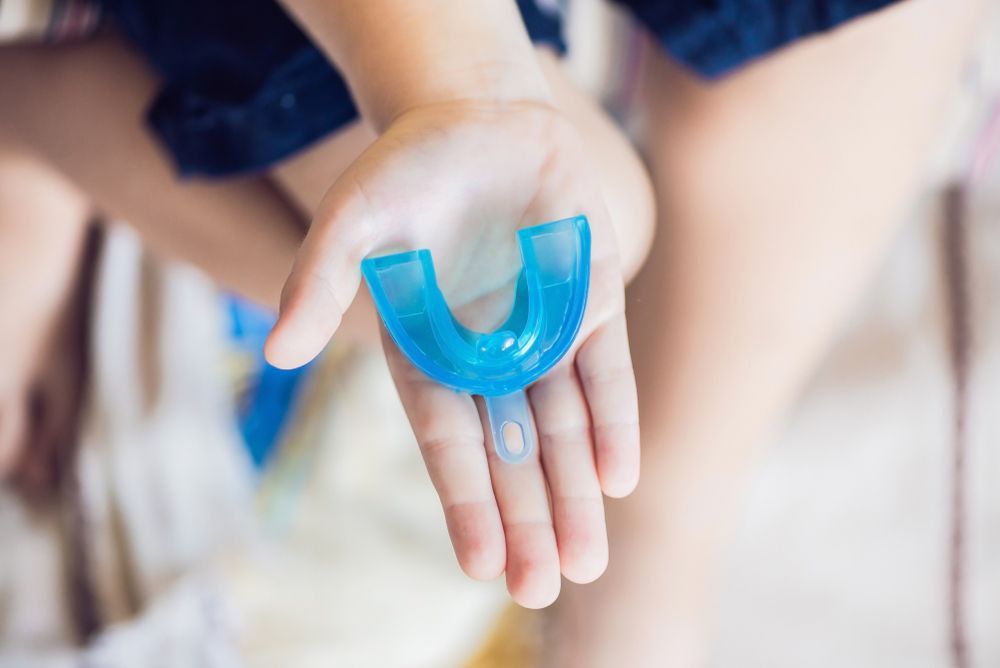 A Child is Holding a Blue Mouth Guard in Their Hand — Parap Family Dental in Parap, NT
