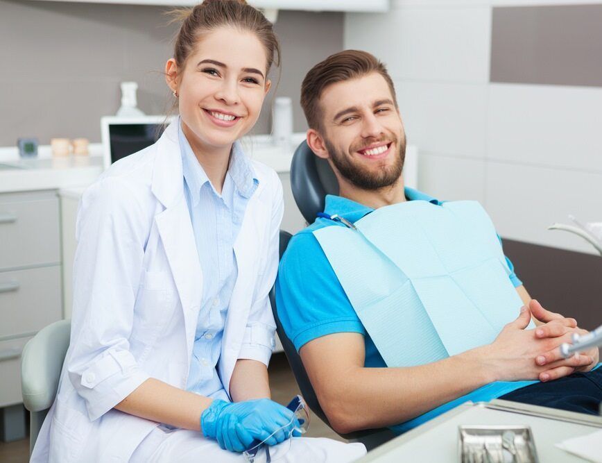 A Man is Sitting in a Dental Chair Next to a Female Dentist — Parap Family Dental in Parap, NT