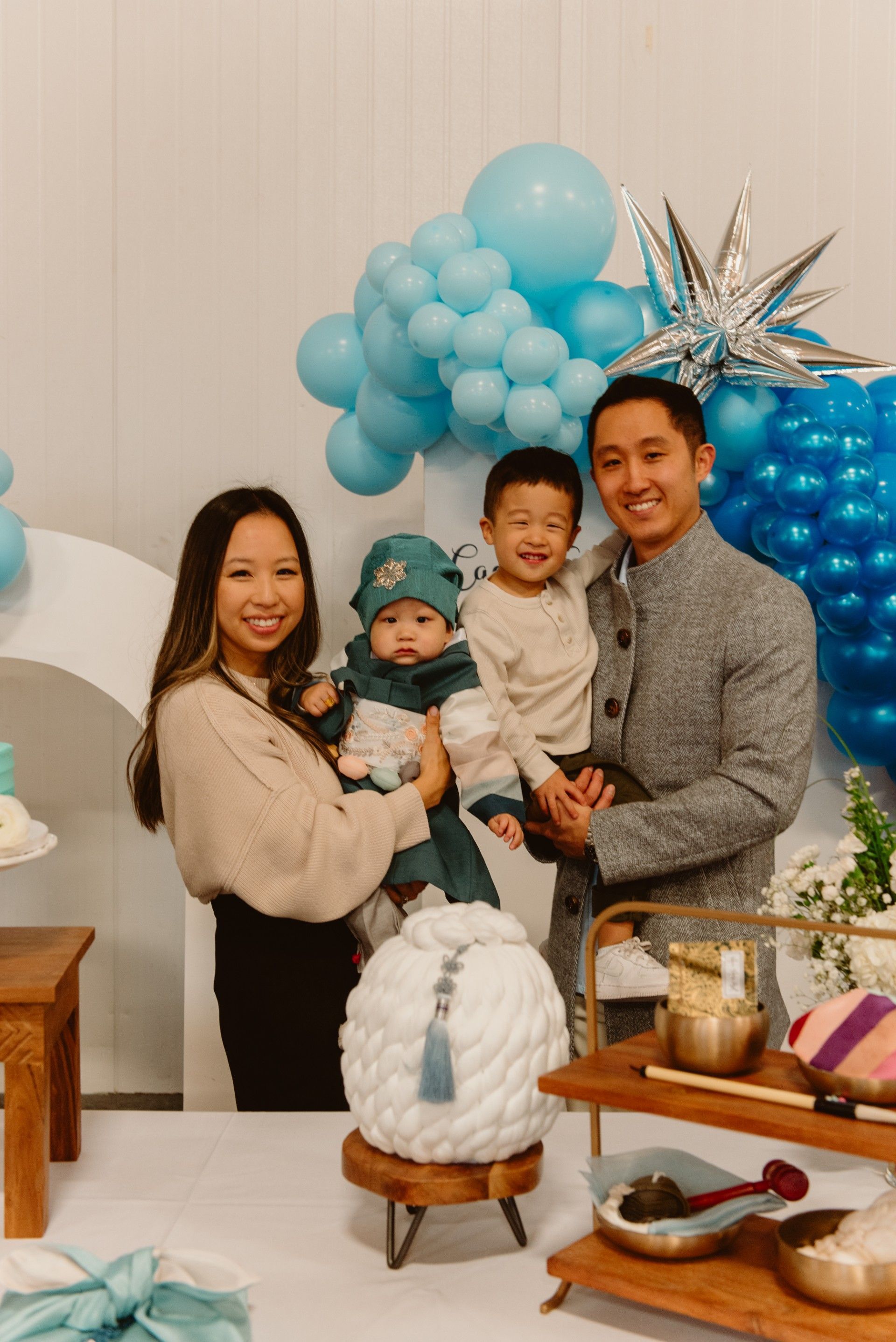 Family of four smiles at camera, posing near blue balloons and a table of food.