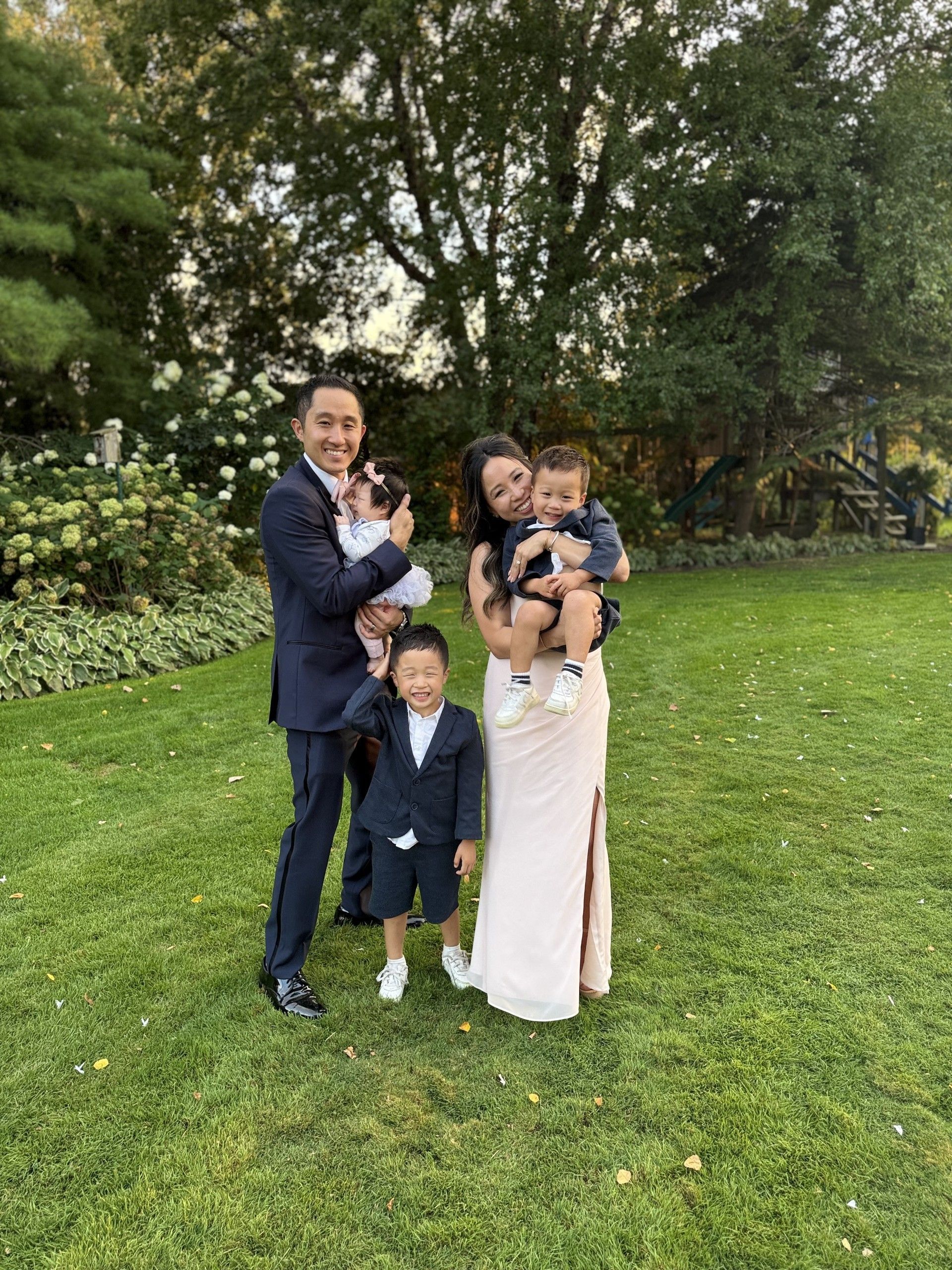 Family of five posing on a lawn, two adults holding toddlers, one child standing.