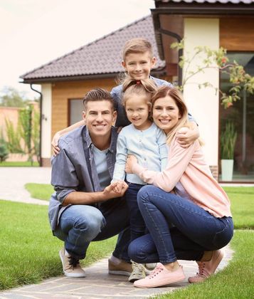 Family of four smiling, posing in front of their house.