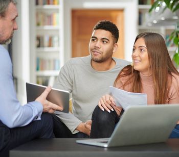 A financial advisor consulting with a couple, reviewing documents and laptop in a home setting.