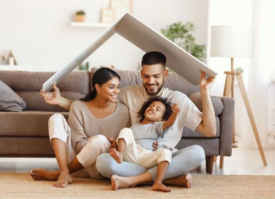 Family of three under a roof shape made of a white material, sitting in a living room.