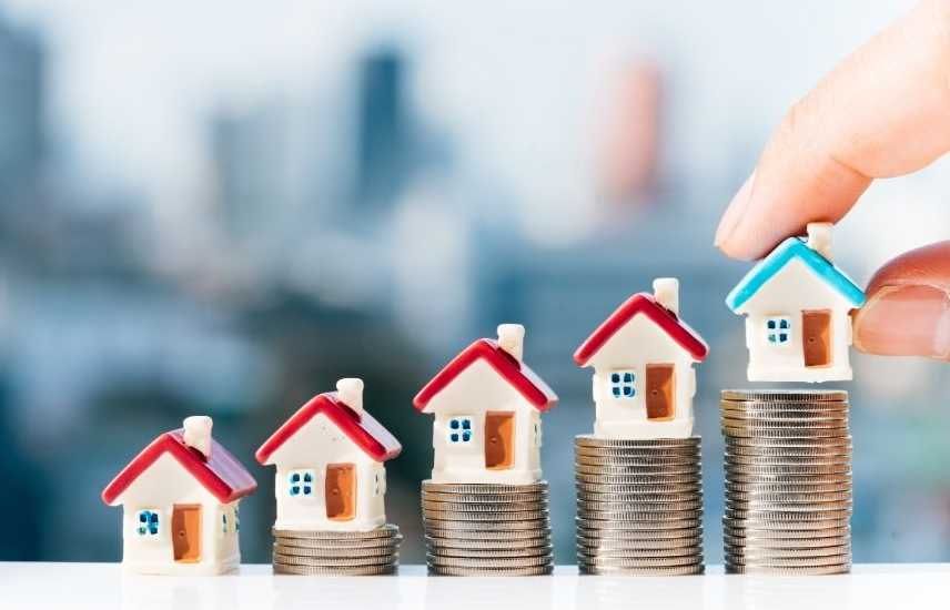 Hand placing a toy house on a stack of coins, representing financial growth in real estate.