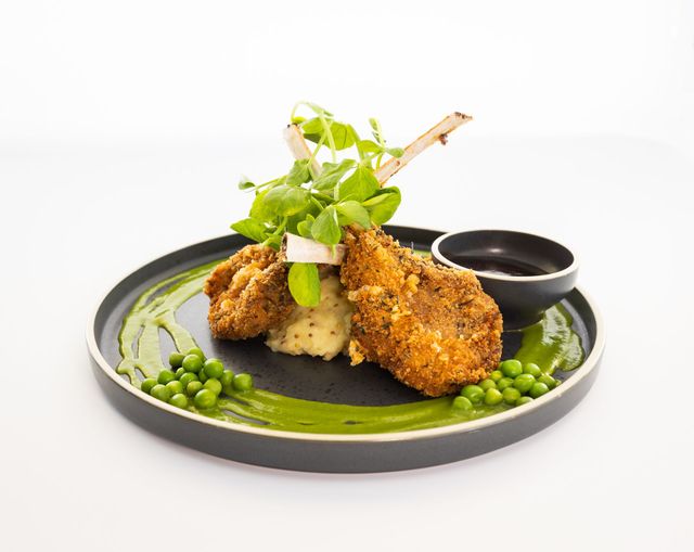 Breaded lamb chops with mashed potatoes, peas, sauce, and greens on a black plate — Jack West Photography In Kawungan, QLD