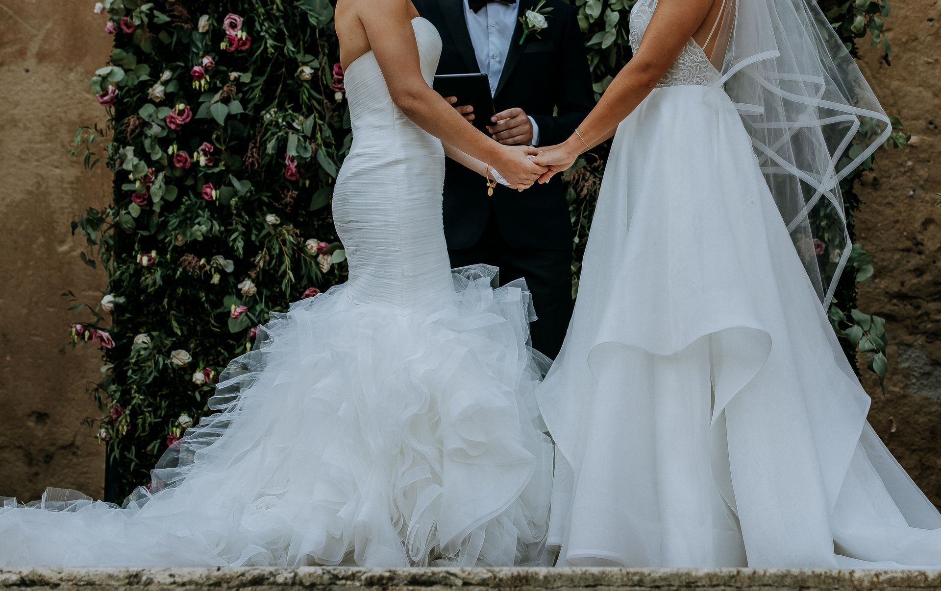 A close-up of a couple holding hands in wedding attire during their ceremony.