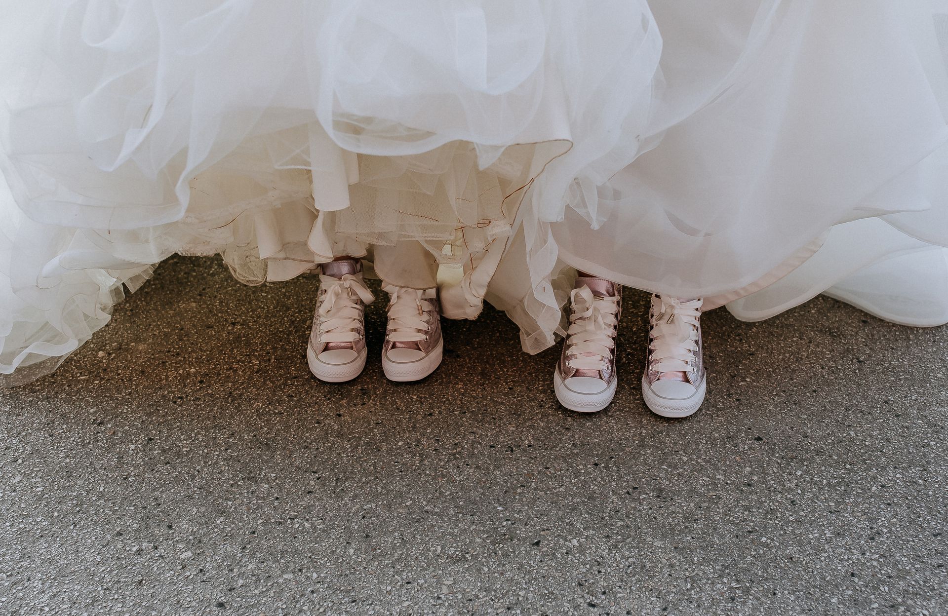 Two brides lifting their gowns to reveal matching pink sneakers.