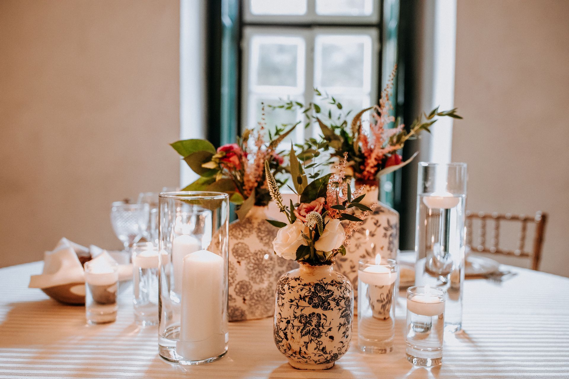 Elegant wedding table setting with floral centerpieces, candles, and natural light from a window.