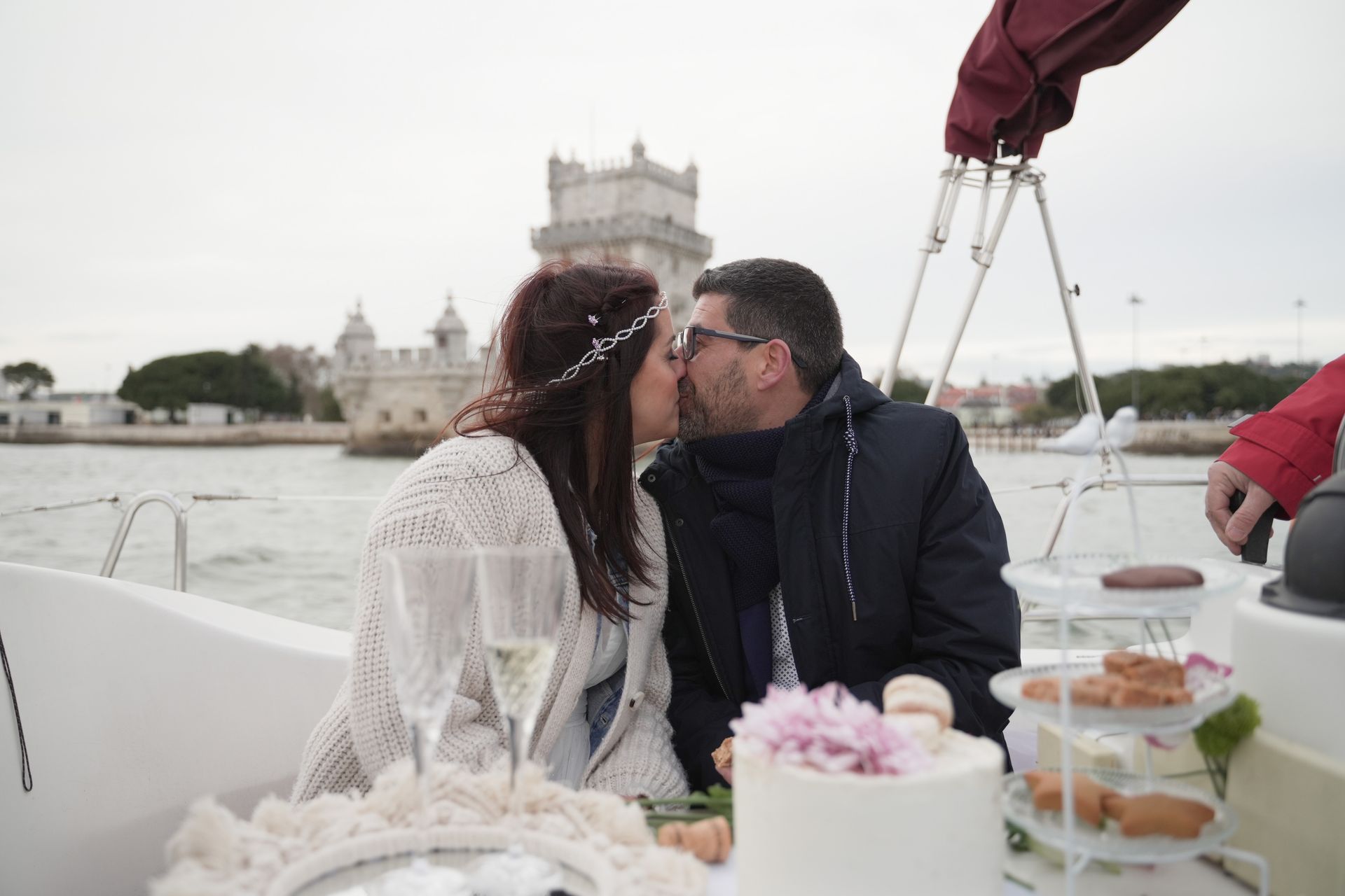 A cozy elopement picnic on a boat near the historic Belém Tower, with a couple in warm attire sharing a kiss.