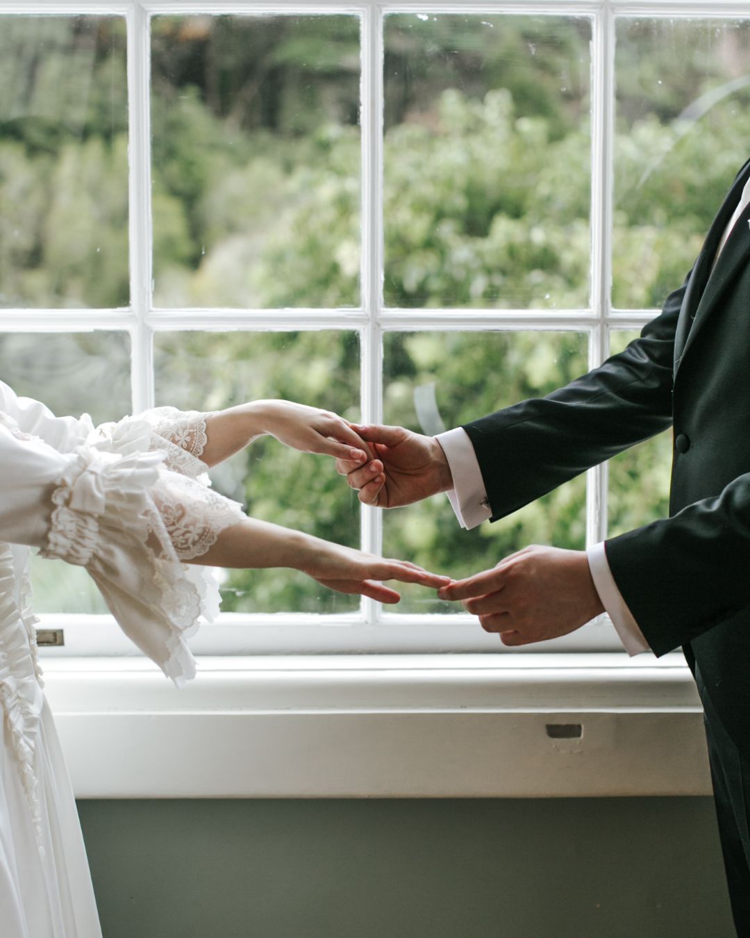 A couple by a bright window, their hands reaching toward each other in a delicate and emotional moment.