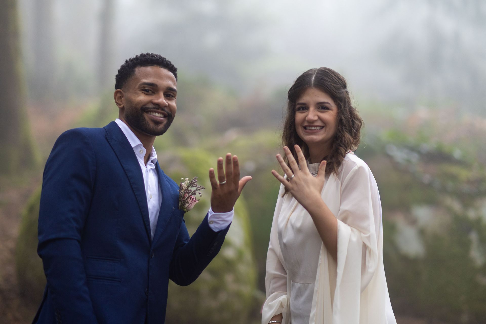 A couple smiling and showing their wedding rings outdoors in misty woodland, Sintra, Portugal