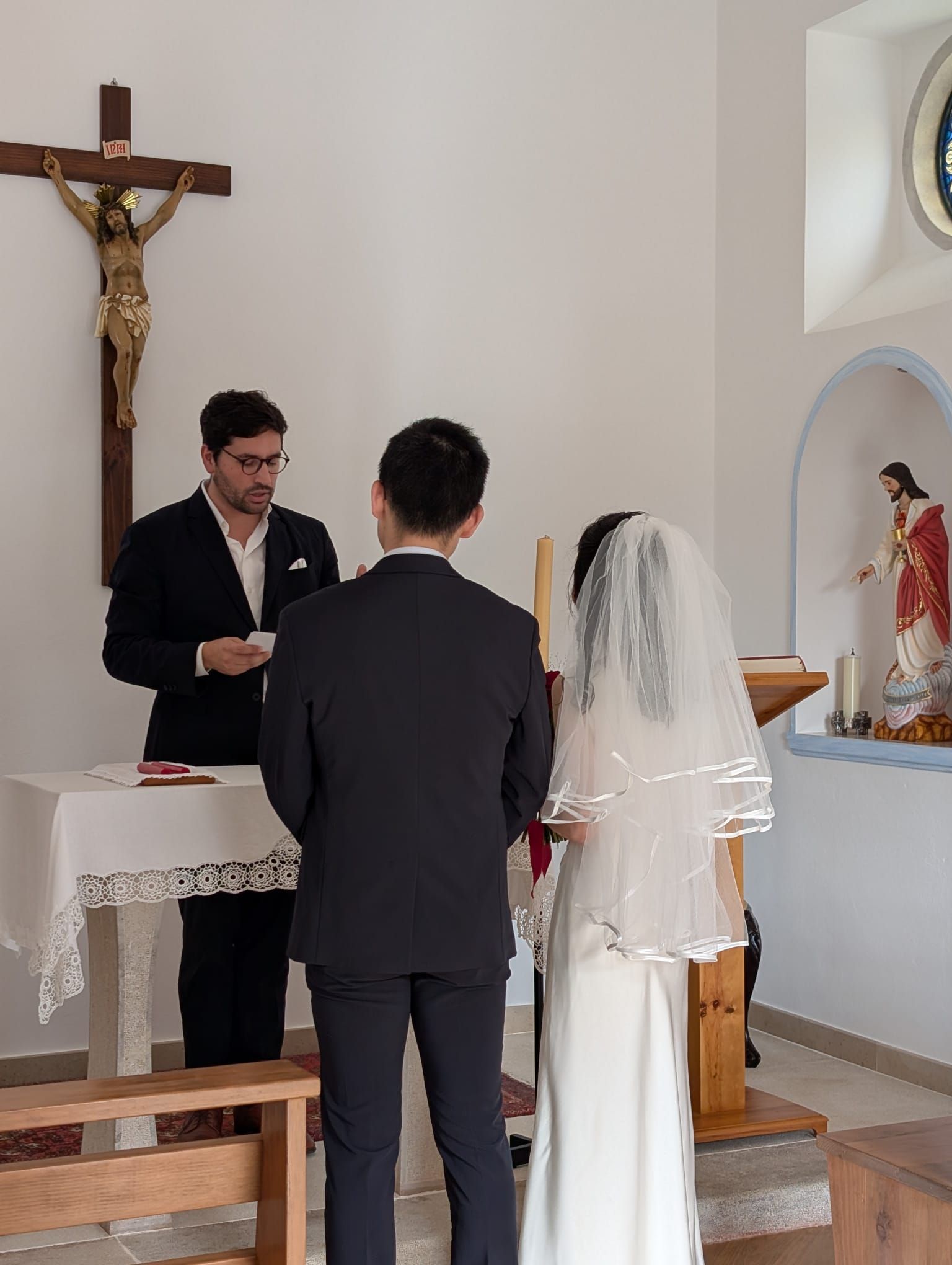 A couple exchanging vows in front of a crucifix during a Catholic wedding ceremony in a Portuguese chapel.