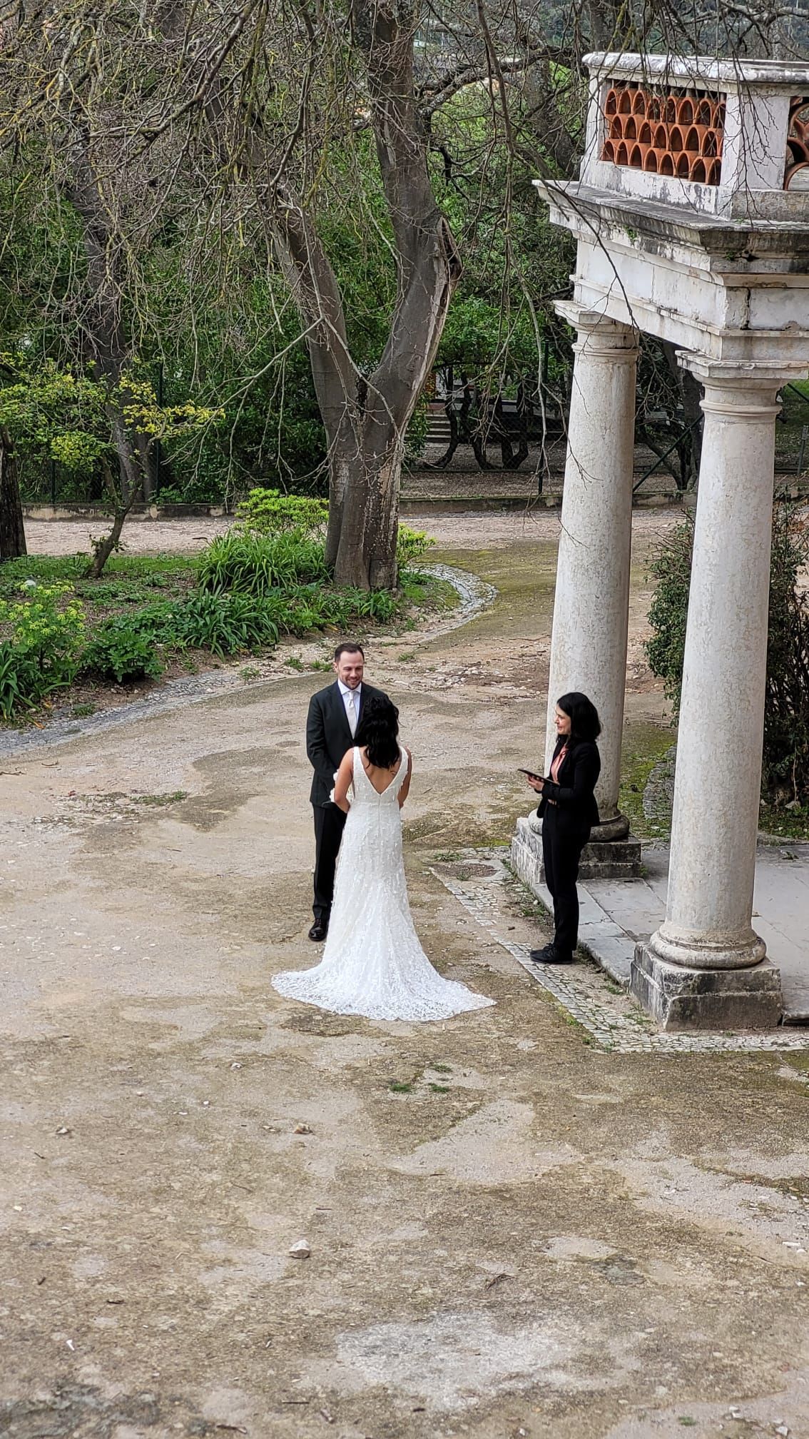 Bride and groom during an outdoor ceremony by stone columns in a peaceful garden setting.