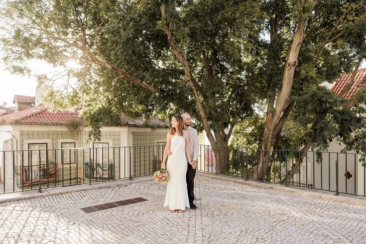 Bride and groom walking hand in hand on a traditional cobblestone street lined with trees.