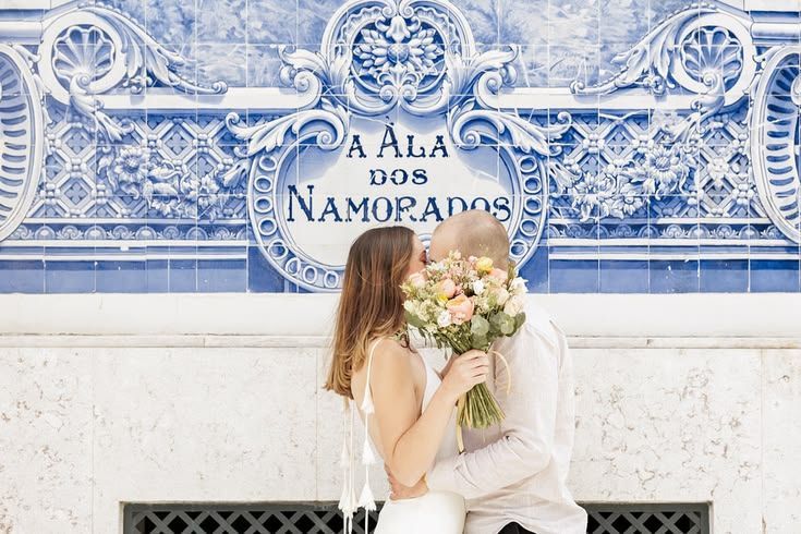 Bride and groom kissing behind a bouquet in front of a traditional blue and white azulejo tile wall, Lisbon.
