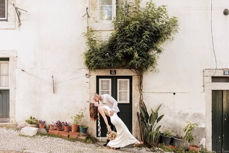Groom dipping bride for a kiss in front of a green door covered in climbing vines.