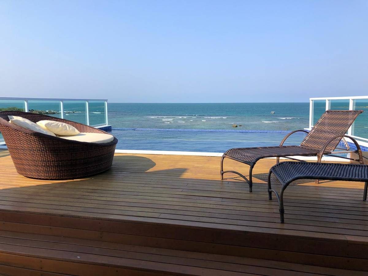 Um deck com cadeiras e espreguiçadeiras com vista para o oceano.
