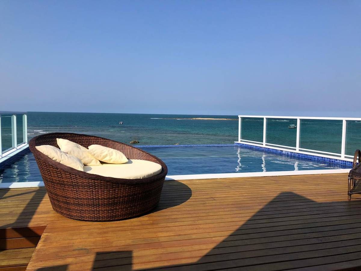 Uma cadeira de vime está sobre um deck de madeira ao lado de uma piscina com vista para o oceano.