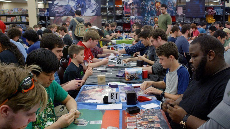 A crowded gaming store with people seated at tables playing a trading card game.