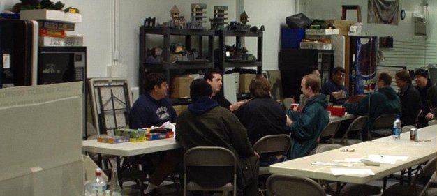 A group of people sits around tables in a hobby shop.