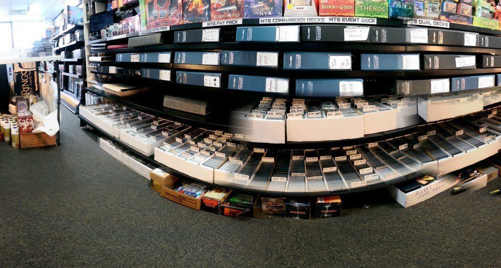 A panoramic shot of shelves in a store filled with organized rows of trading cards in white boxes and various binders.
