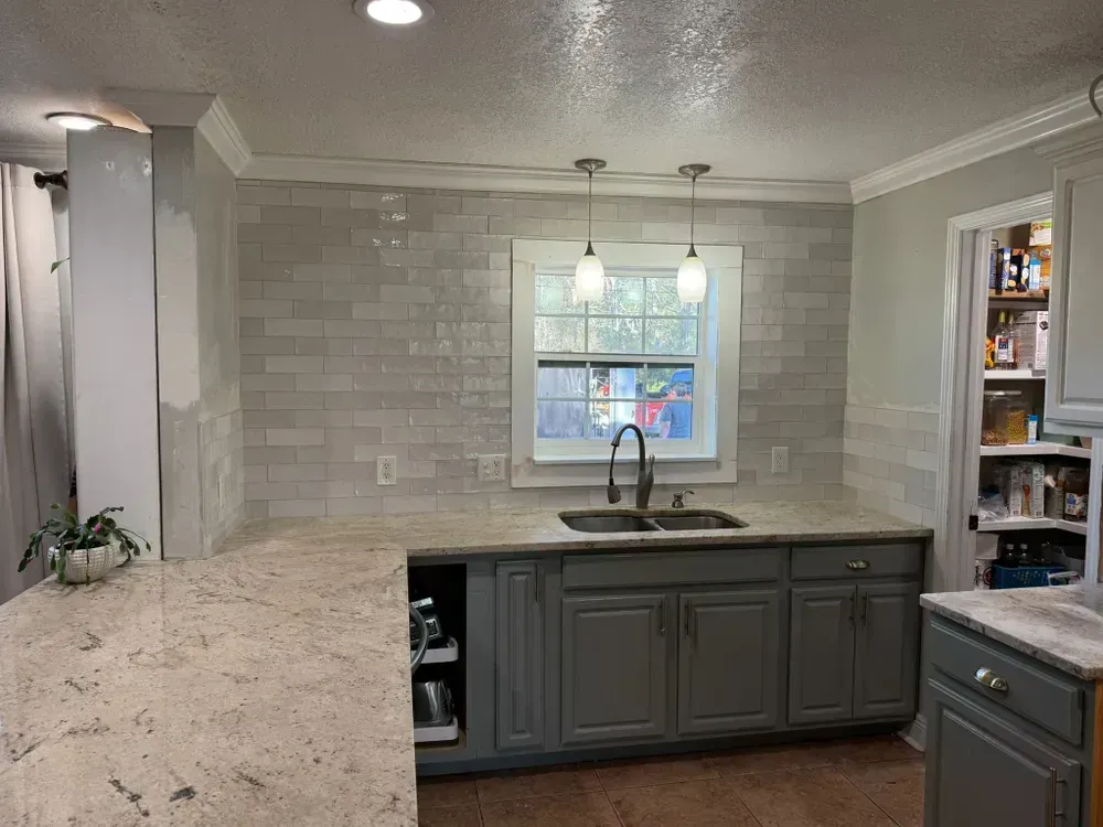 A kitchen with gray cabinets , granite counter tops , a sink and a window.