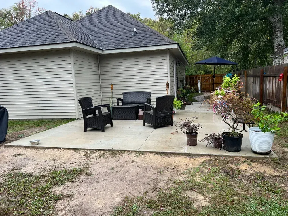 A patio with a couch , chairs , umbrella and potted plants in front of a house.
