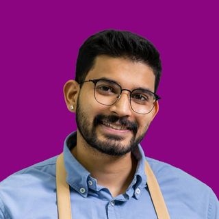 Smiling person with glasses and apron against a purple background