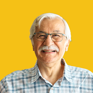 Smiling man with glasses and white hair against a bright yellow background