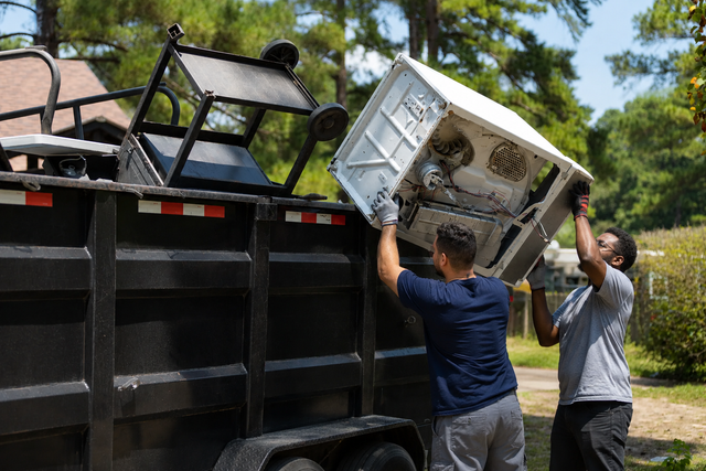 Two people lifting a white appliance into the bed of a black truck outdoors