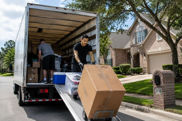 People unloading furniture and boxes from a moving truck in a suburban driveway