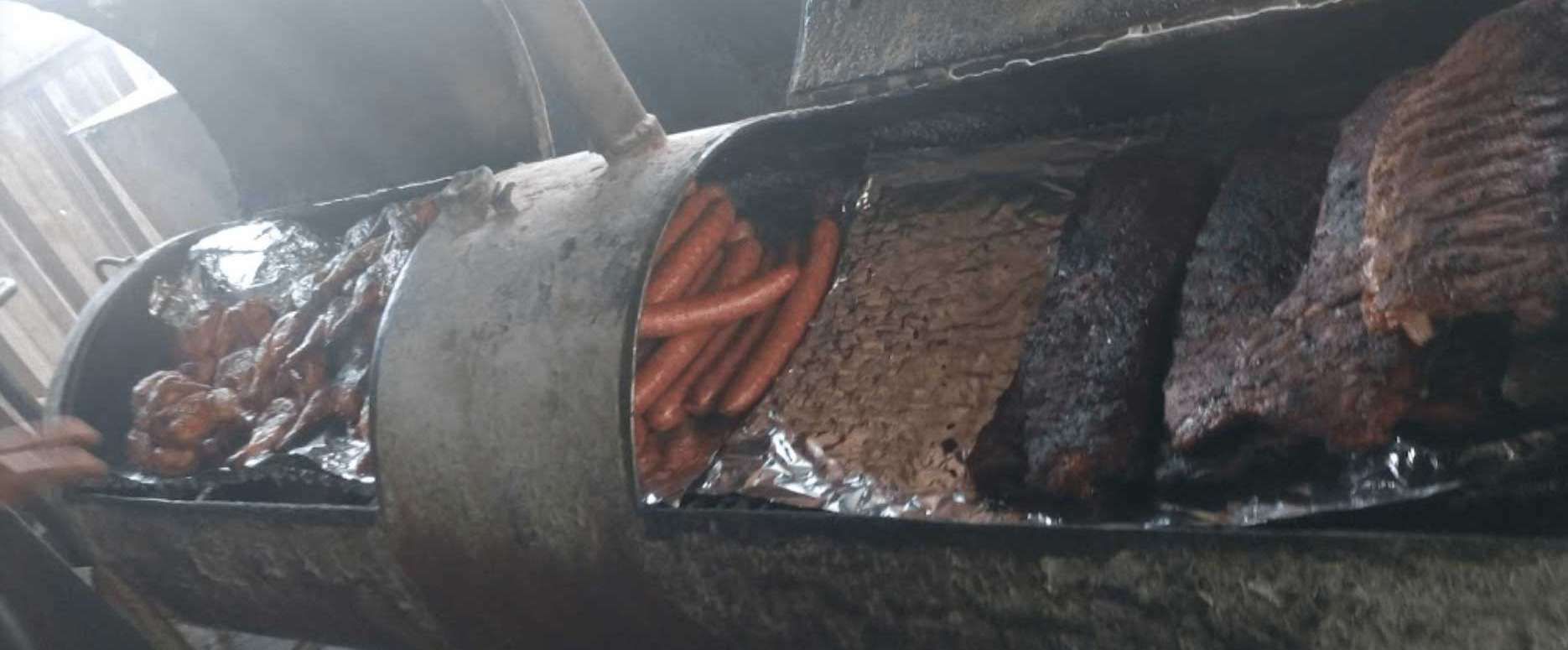 Smoked meat and sausages on a grill, wrapped in foil and resting over red coals.