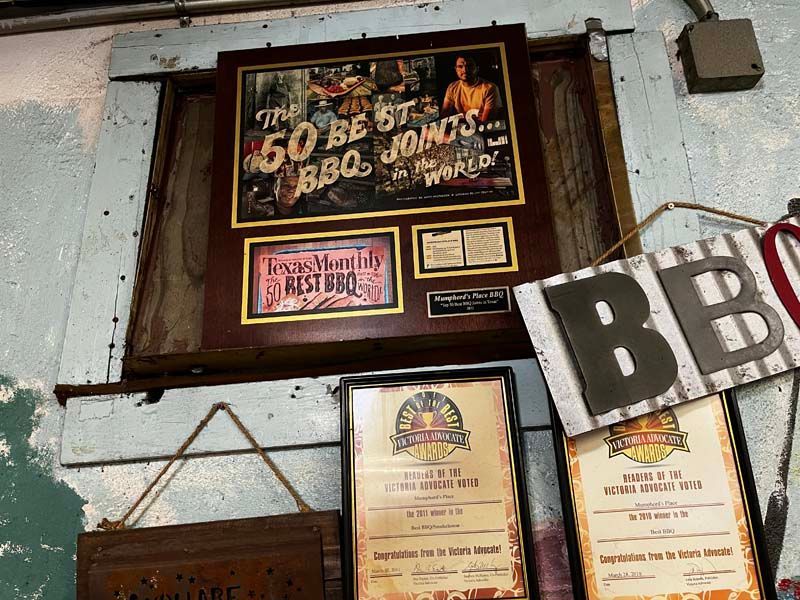 Wall of framed awards and signs in a rustic interior, with large black-and-white letters in the foreground