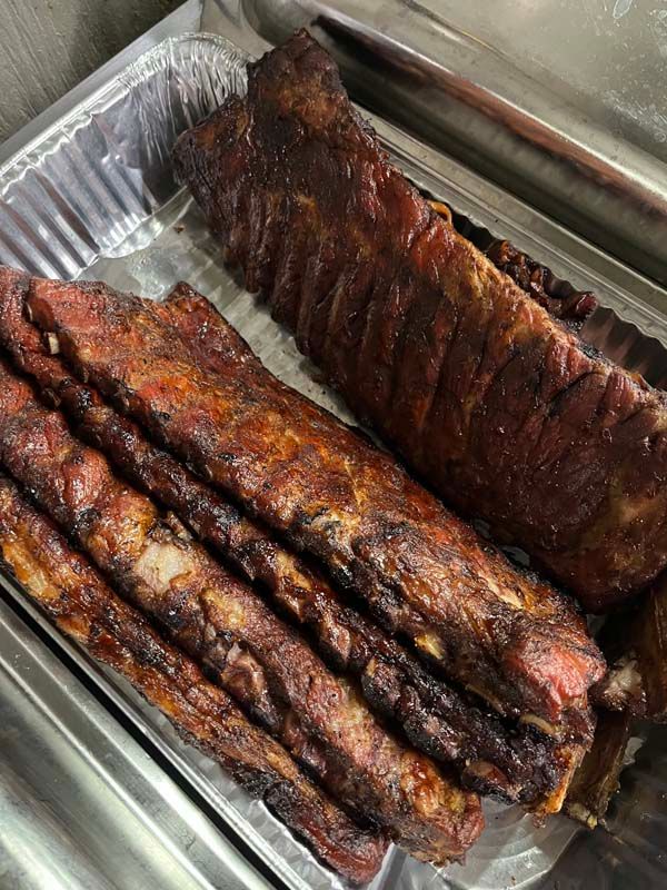 Tray of glazed smoked ribs in a metal pan at a food counter